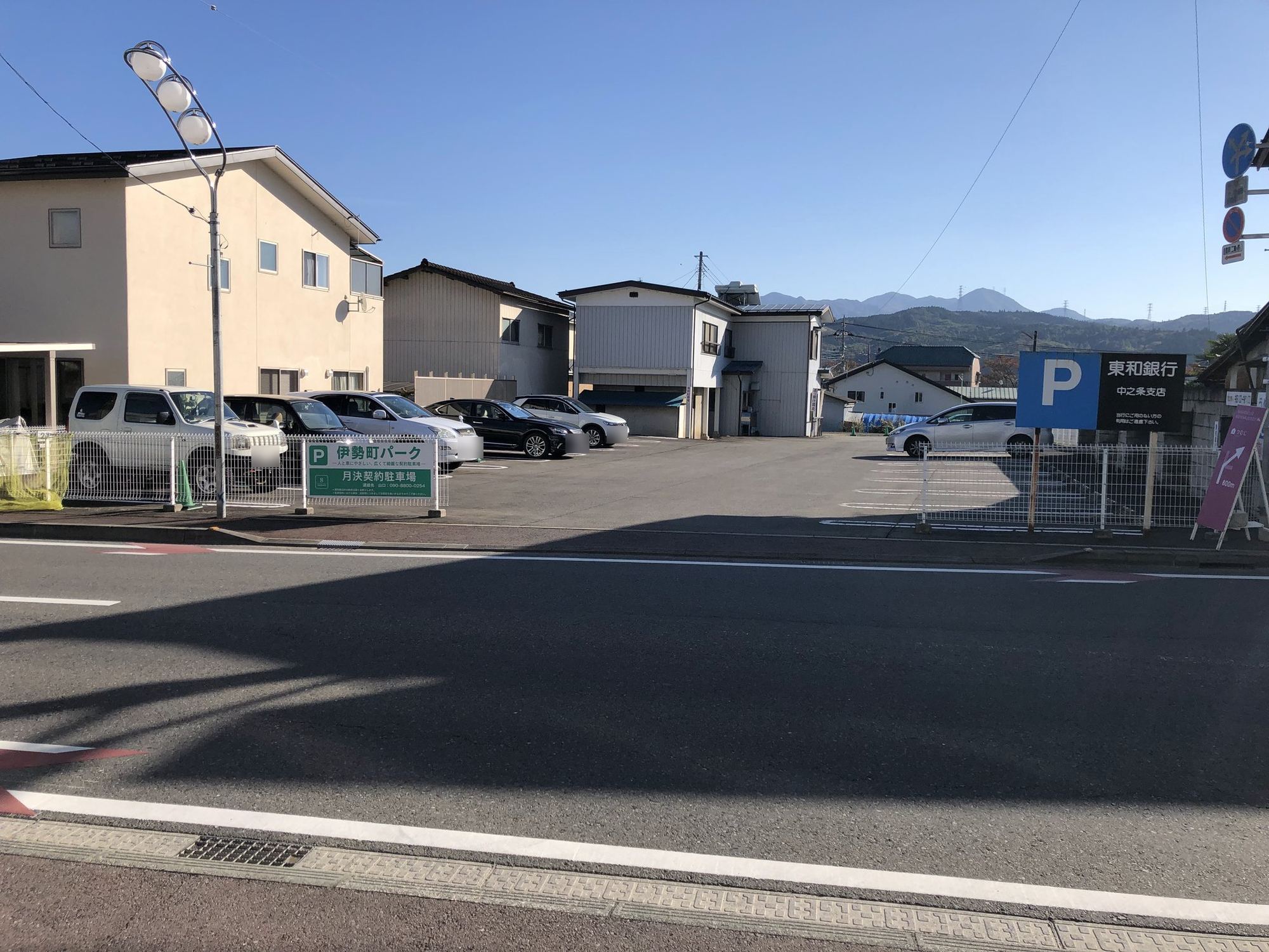 道路側から見た伊勢町パークの全景。白線で区画された平面駐車場と「伊勢町パーク」の看板、奥に山並み。